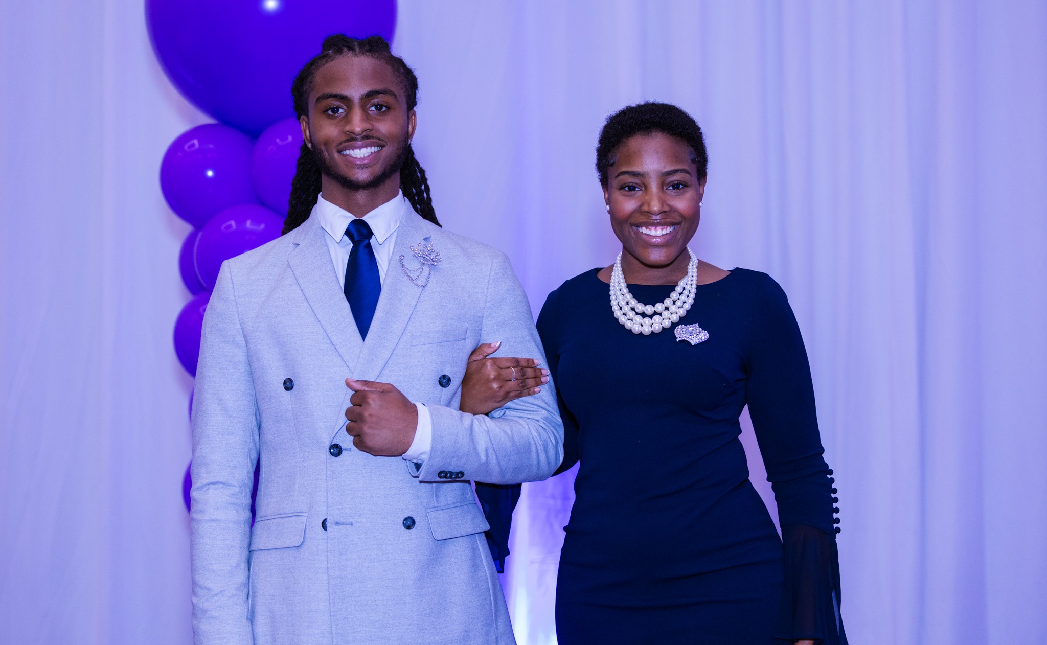 Two people posing for photo in front of a lavender colored background